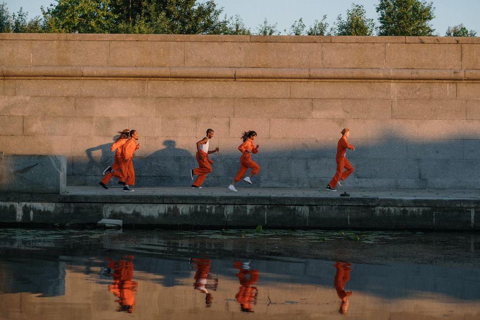 Grupo de pessoas treinando corrida ao ar livre, vestindo roupas esportivas laranja sob a luz do pôr do sol.