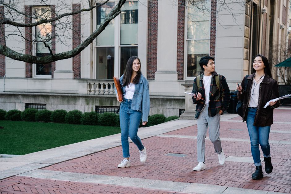 Estudantes universitários caminhando e conversando ao ar livre em um campus acadêmico, promovendo interação social e aprendizado.