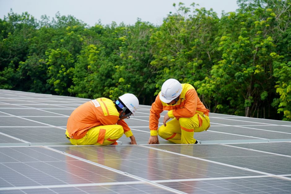 Técnicos realizando manutenção em painel de energia solar em área ao ar livre com vegetação ao fundo.