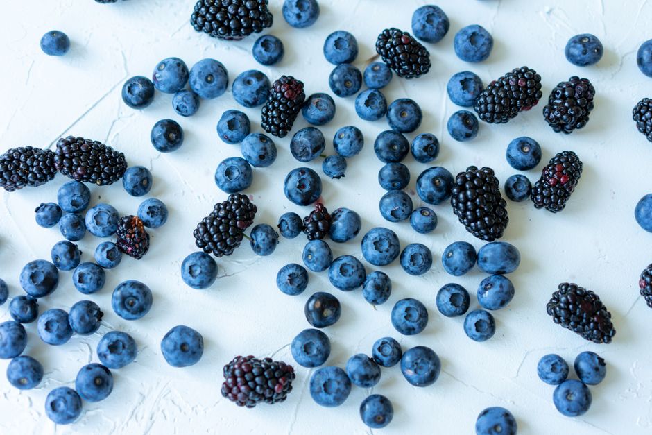 Imagem de mirtilos e amoras espalhados sobre uma superfície clara, destacando a origem natural das frutas silvestres.