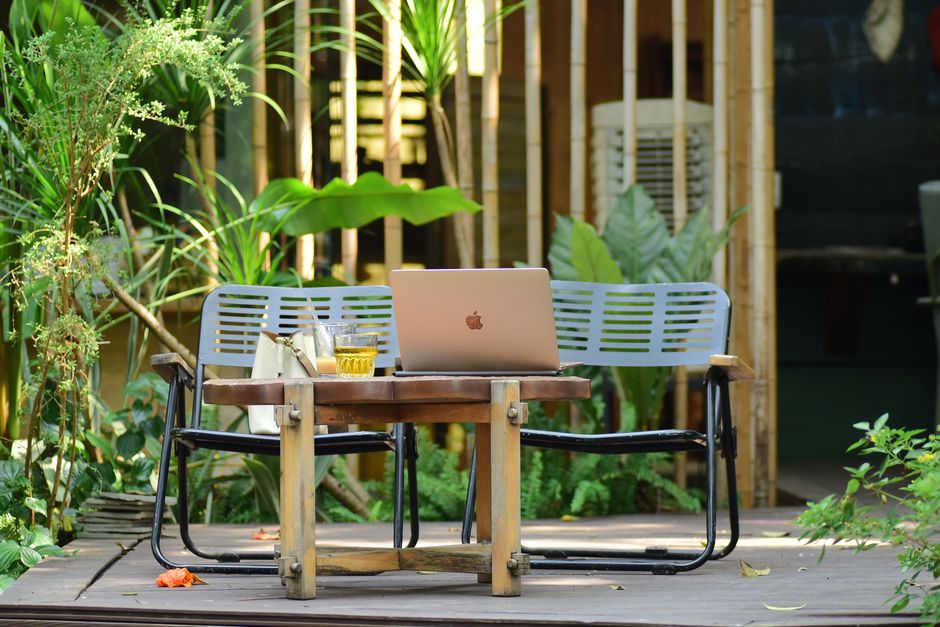 Ambiente de trabalho ao ar livre com um laptop em uma mesa de madeira, cercado por plantas verdes, ideal para artigos sobre produtividade em ambientes naturais ou coworking ao ar livre.