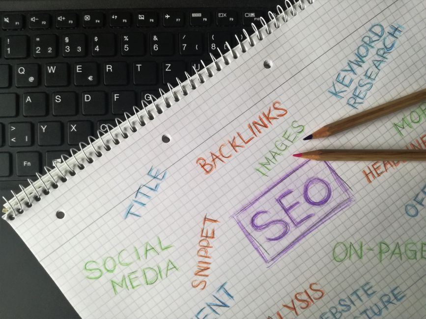 Notas de planejamento de SEO com anotações coloridas sobre backlinks, palavras-chave e estratégias de marketing digital ao lado de um teclado de computador.