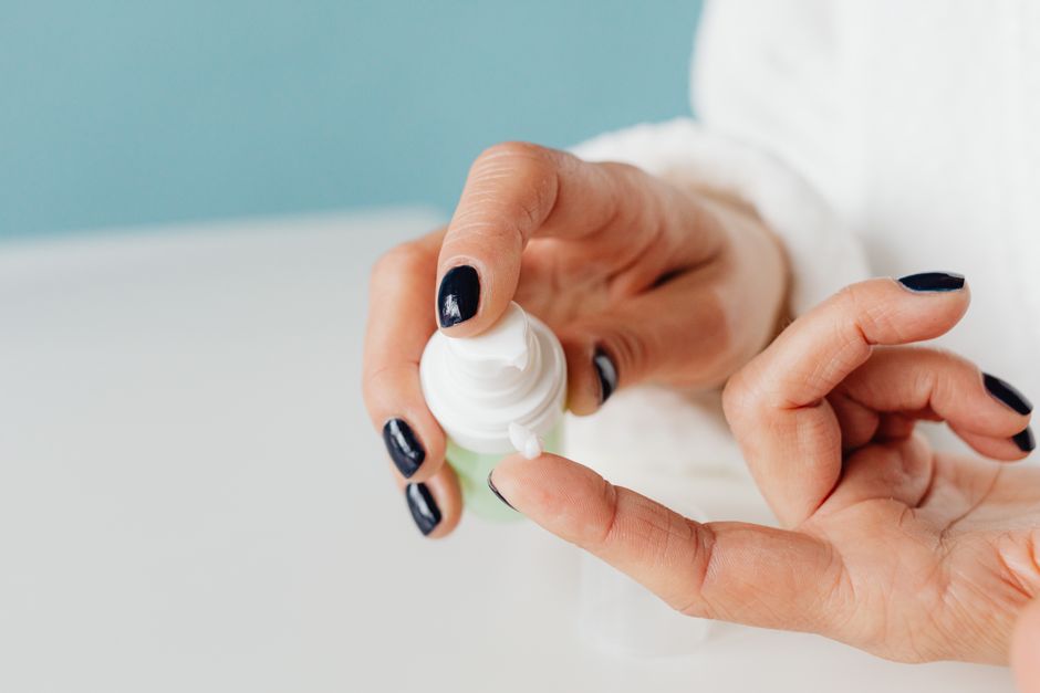 Mulher aplicando creme em seus dedos, simbolizando autocuidado e rotina de beleza.