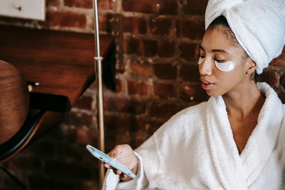 Mulher relaxando após banho, usando roupão e toalha na cabeça, com olhos de descanso e expressão de bem-estar, em ambiente acolhedor e confortável.