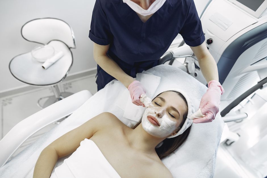 Mulher recebendo tratamento de spa facial em ambiente de clínica de estética, com profissional aplicando produtos e equipamentos de cuidados com a pele.