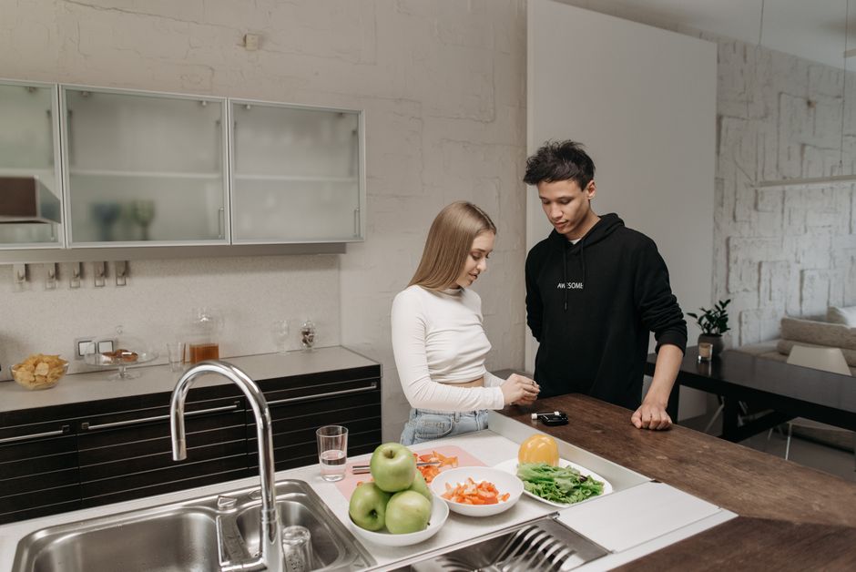 Jovens conversando na cozinha moderna, com alimentos frescos e utensílios ao redor, em um ambiente acolhedor e contemporâneo.