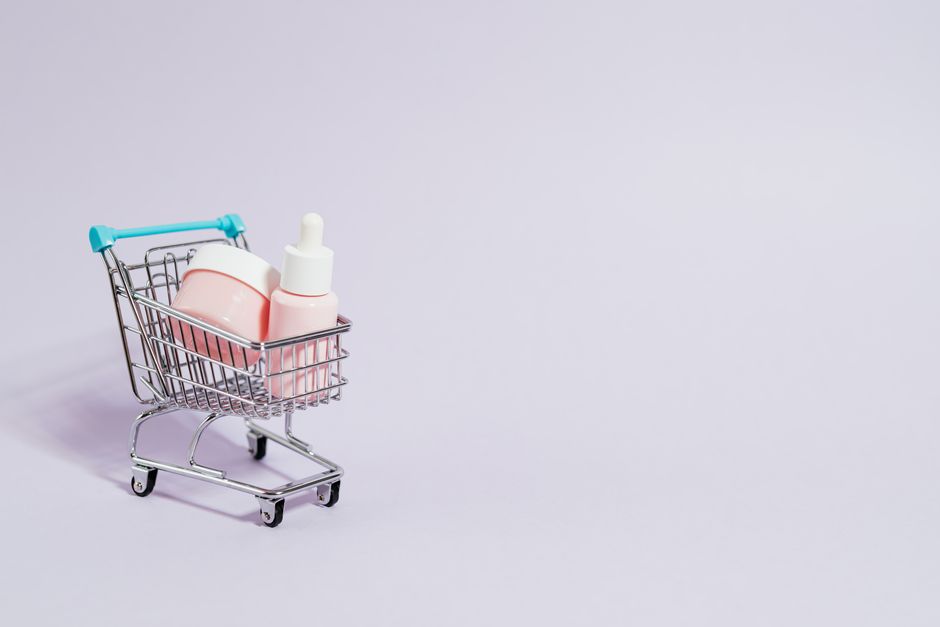 Imagem conceitual de um carrinho de supermercado miniatura contendo produtos de beleza, simbolizando cuidados pessoais ou cosméticos na rotina diária.