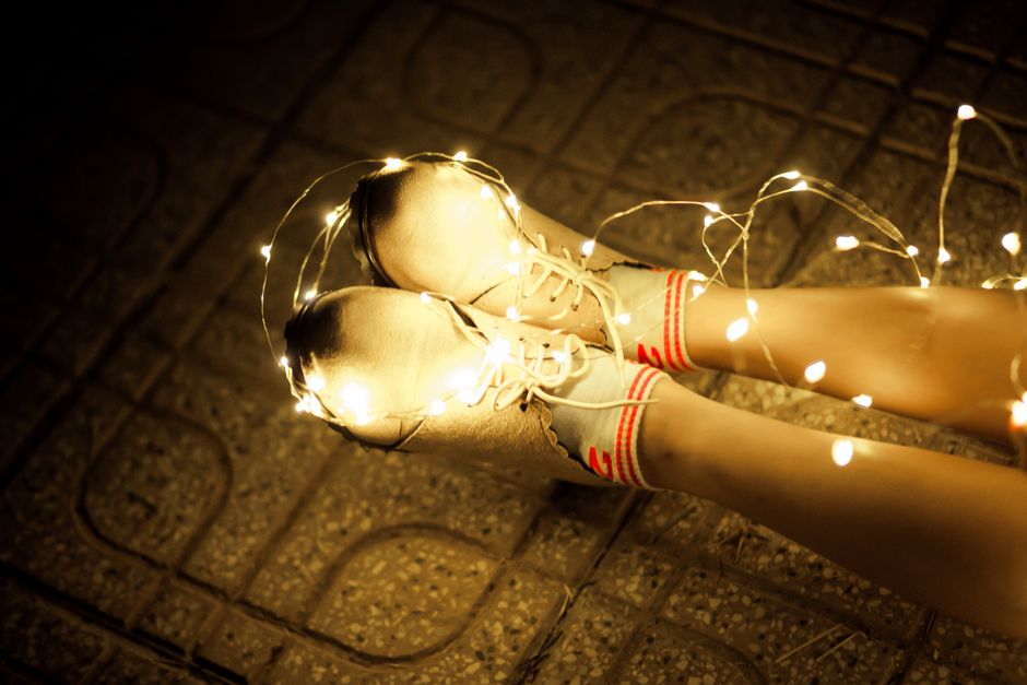 imagem de pernas femininas usando tênis e meias com riscas vermelhas, com luzes decorativas ao redor, sugerindo criatividade ou expressão artística em um ambiente externo