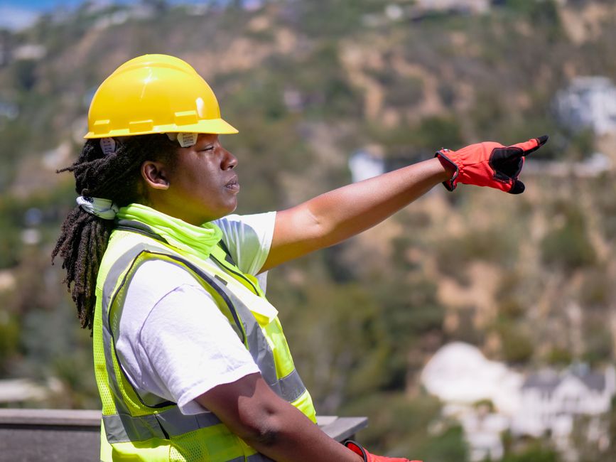 Profissional de construção civil orientando em obra ao ar livre, destacando liderança e segurança.