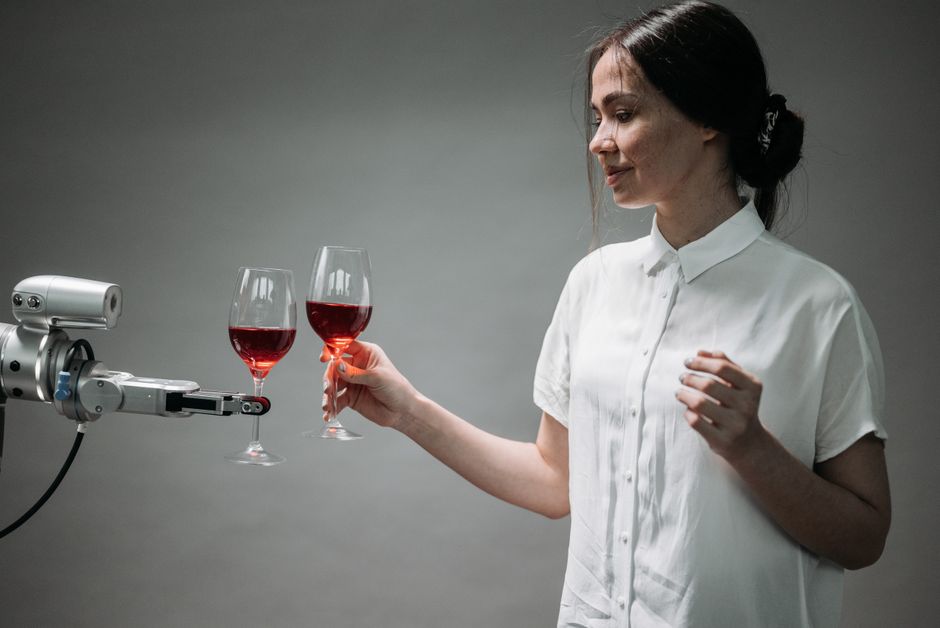 Mulher brindando com taças de vinho ao lado de um robô, simbolizando tecnologia e inovação em experiências sociais ou degustação assistida por inteligência artificial.