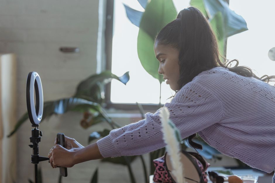Mulher ajustando iluminação para gravação de vídeo em ambiente interno com plantas ao fundo, ideal para conteúdo digital ou influenciador digital.