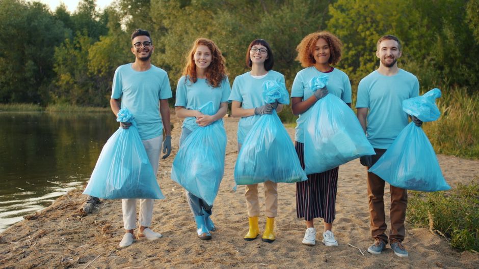 Grupo de jovens participando de uma ação de limpeza ambiental às margens de um rio, destacando o tema de sustentabilidade e preservação do meio ambiente.