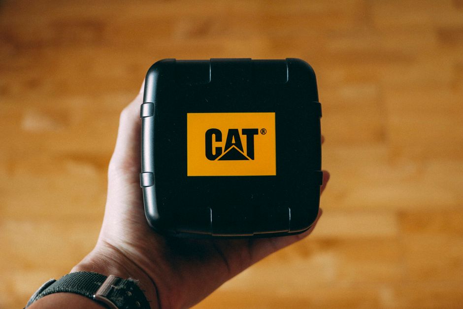 Imagem de uma mão segurando uma caixa preta com o logotipo da CAT, símbolo de equipamentos pesados e maquinário industrial.