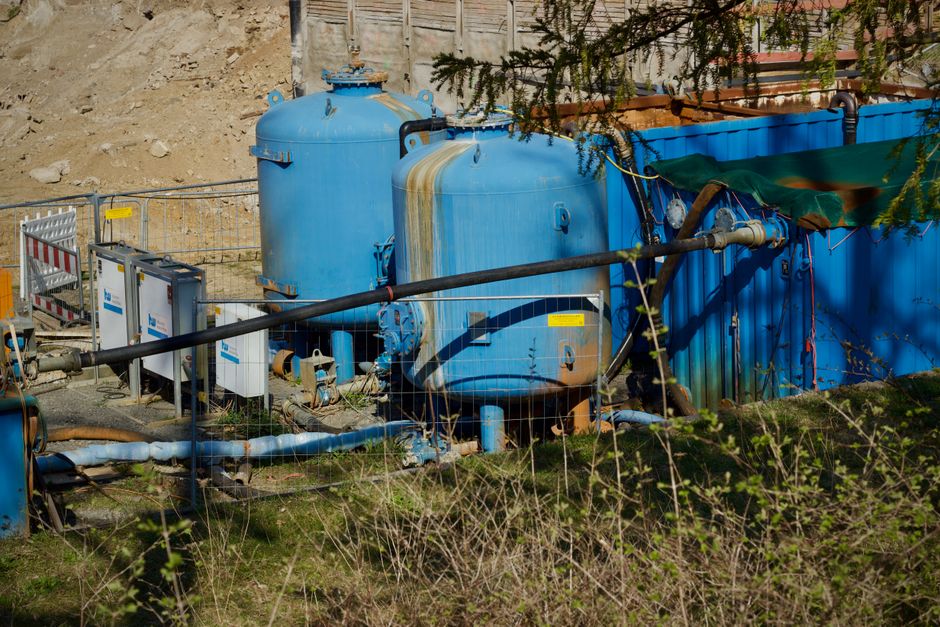 Imagem de uma instalação de sistema de captação de água de chuva com tanques azuis em um local externo, cercado por elementos de proteção e vegetação ao redor.