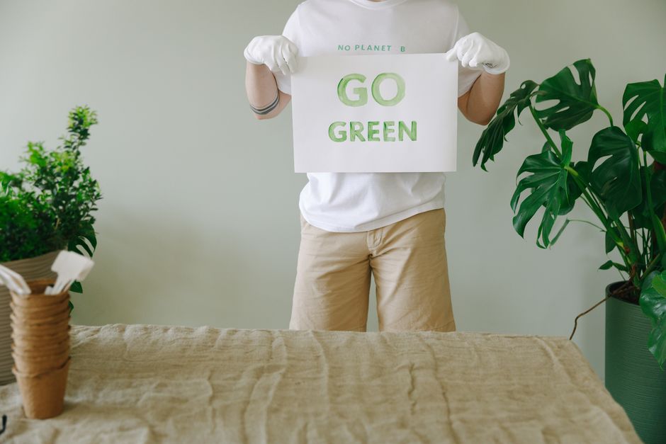 Pessoa segurando um cartaz com a mensagem 'GO GREEN', promovendo consciência ambiental e sustentabilidade.