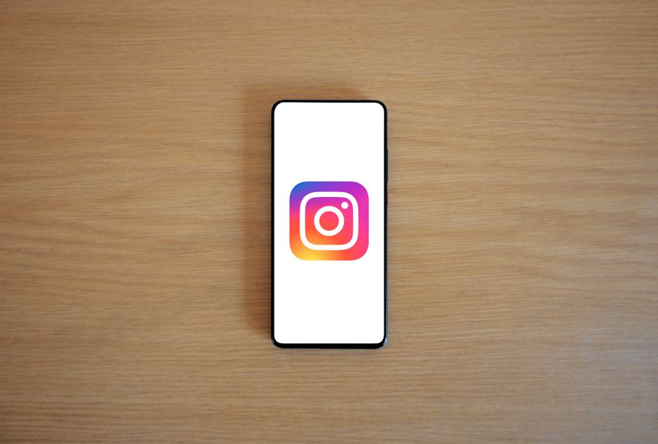 Imagem de um smartphone com o logotipo do Instagram na tela, posicionado sobre uma superfície de madeira plana, sugerindo uso de redes sociais e marketing digital.