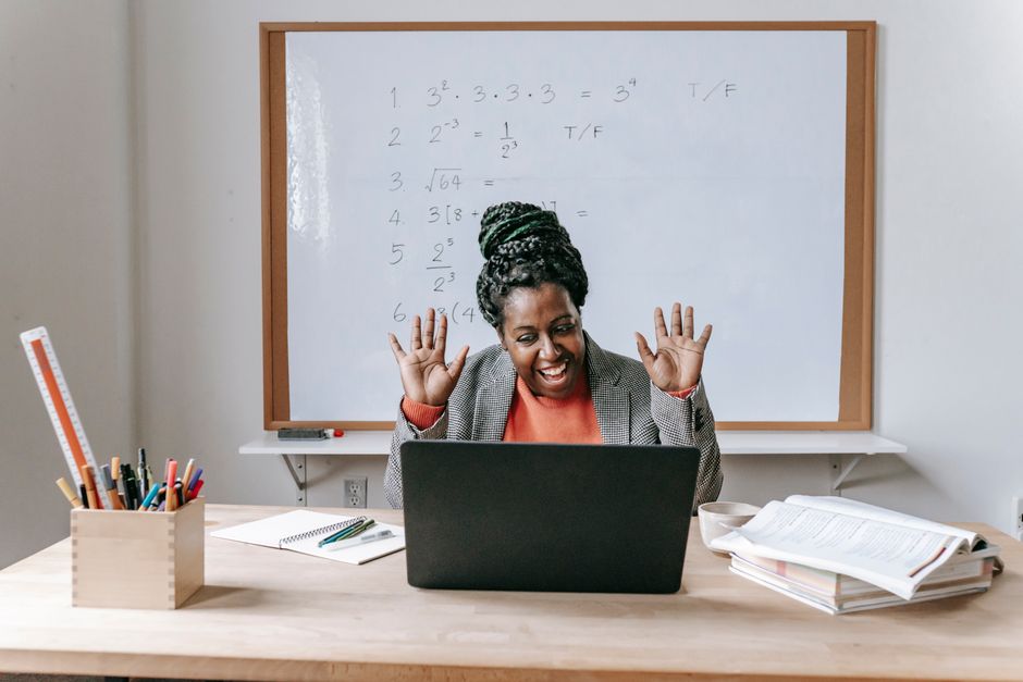Professora entusiasmada durante aula online de matemática, usando computador em um ambiente de sala de aula.