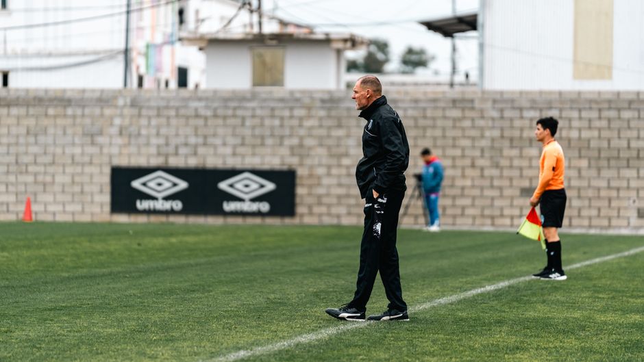 Treinador observando uma partida ou treino de futebol em um campo ao ar livre.