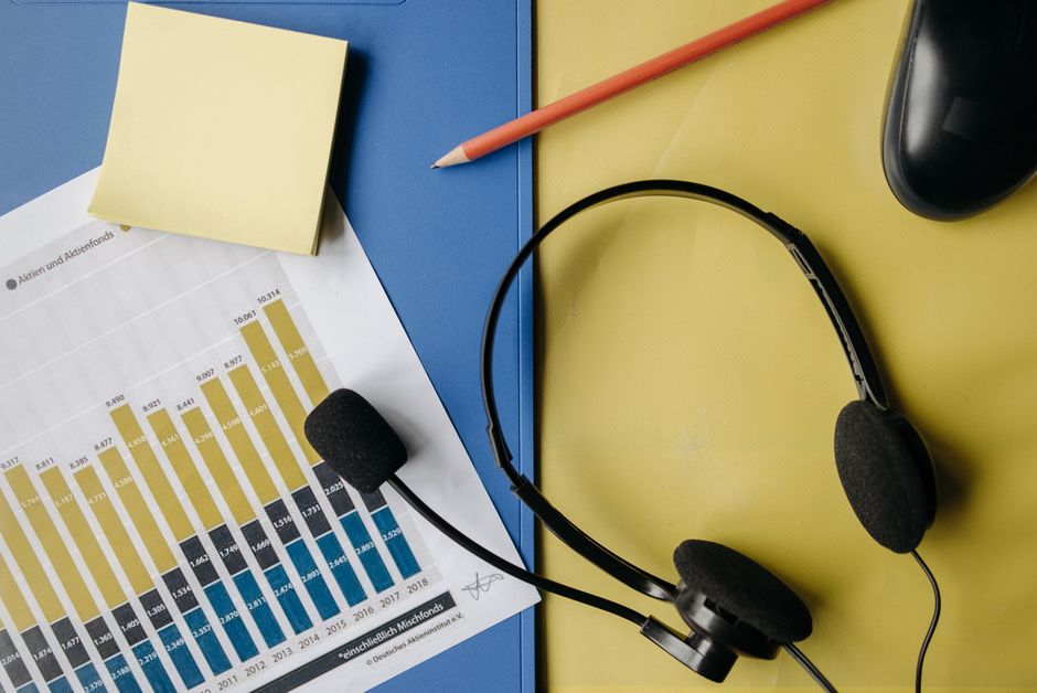 Imagem de uma estação de trabalho com gráficos de negócios, fones de ouvido, caderno, caneta e objetos de escritório, ideal para artigos sobre comunicação empresarial ou análise de dados.