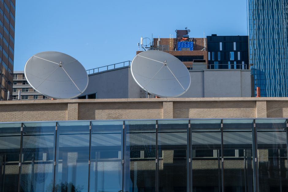 Imagem de edifícios empresariais modernos com antenas parabólicas no topo, simbolizando tecnologia e comunicação urbana.