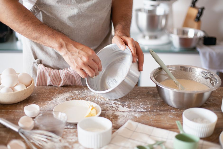 Pessoa preparando massa para uma receita de cozinha, com ingredientes e utensílios em uma bancada rústica.