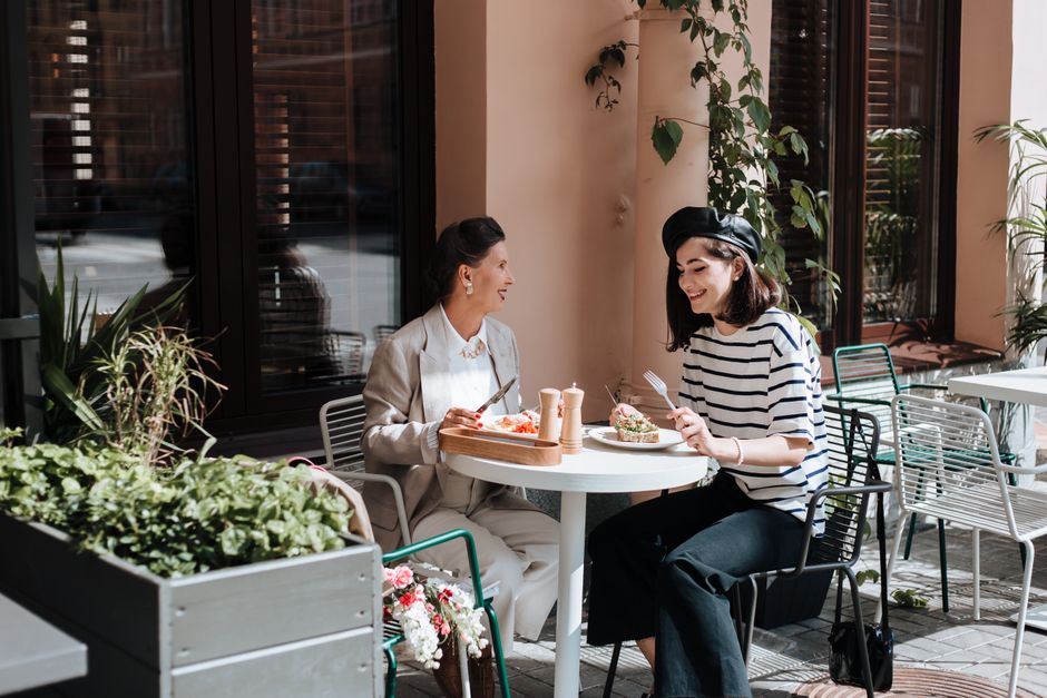 Duas mulheres sorridentes desfrutando de um almoço ao ar livre em um ambiente acolhedor de café, promovendo conexão social e lazer.