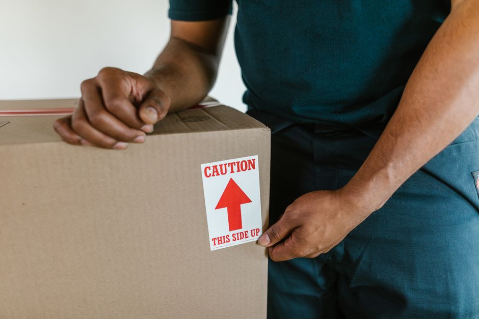 Pessoa manuseando uma caixa de papelão com atenção, sugerindo cuidado e segurança na logística ou transporte de produtos.