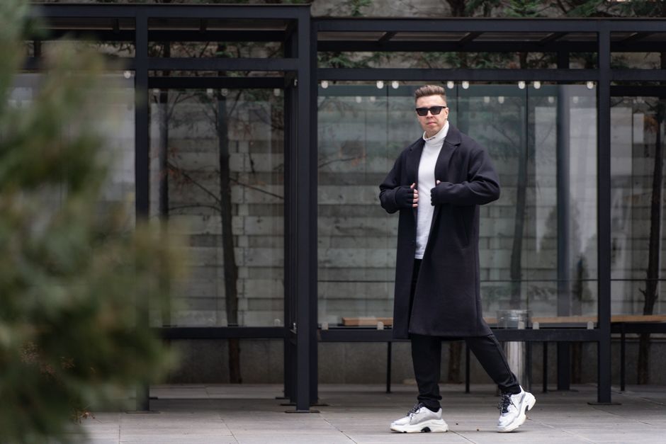 Homem estiloso posando ao ar livre com expressão confiante, representando moda e estilo urbano.