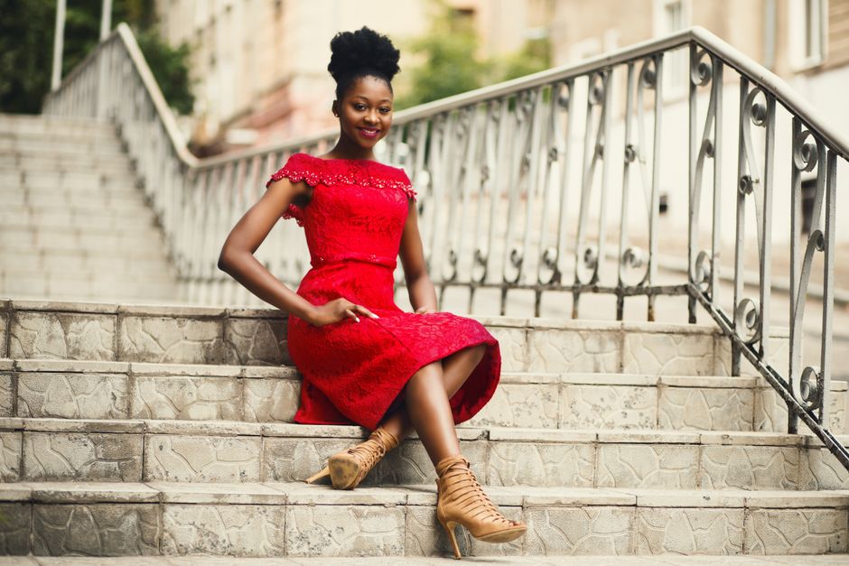 Mulher sorridente vestindo um vestido vermelho sentado em escadas externas, transmitindo elegância e confiança para um artigo sobre moda e estilo de vida.