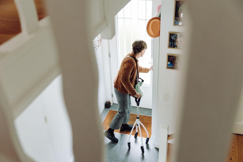 Imagem de uma pessoa com deficiência usando uma andadora na entrada de uma casa moderna, simbolizando acessibilidade e inclusão social.