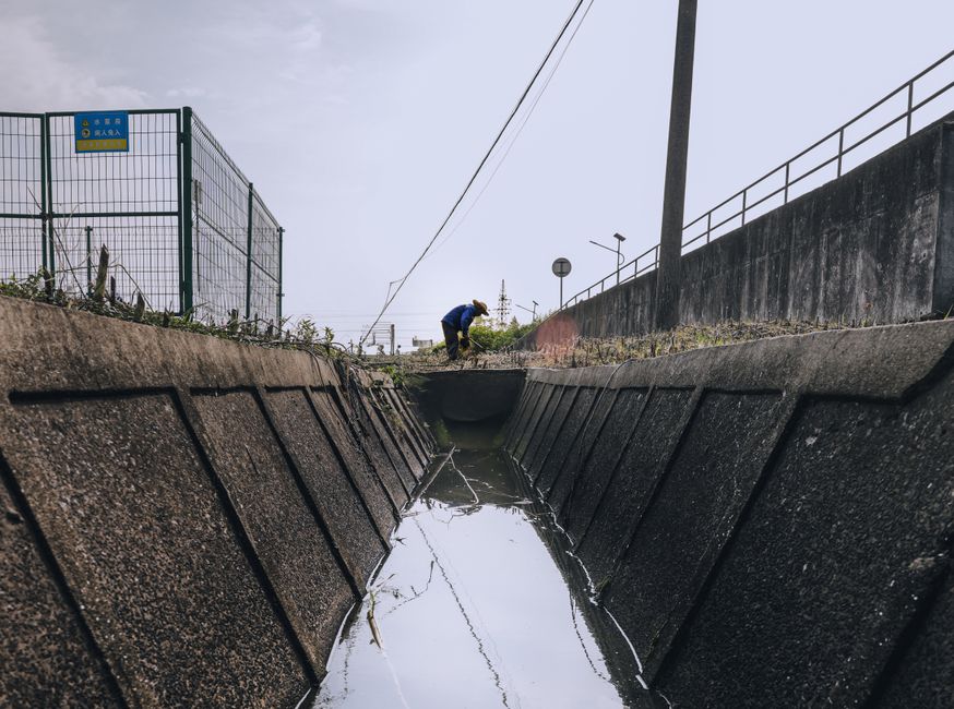 Pessoa realizando inspeção ou manutenção em um canal de drenagem urbano, com foco na área de infraestrutura e controle de água pluvial.
