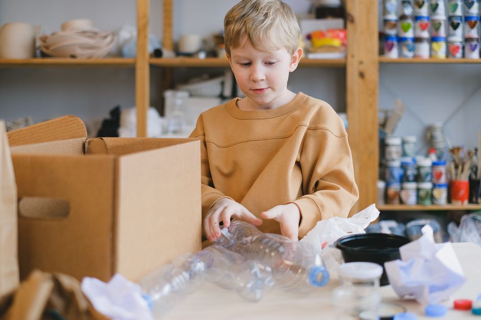 Juiz de menor observando uma garotinha embalando materiais recicláveis em um ambiente artesanal ou de coleta seletiva.