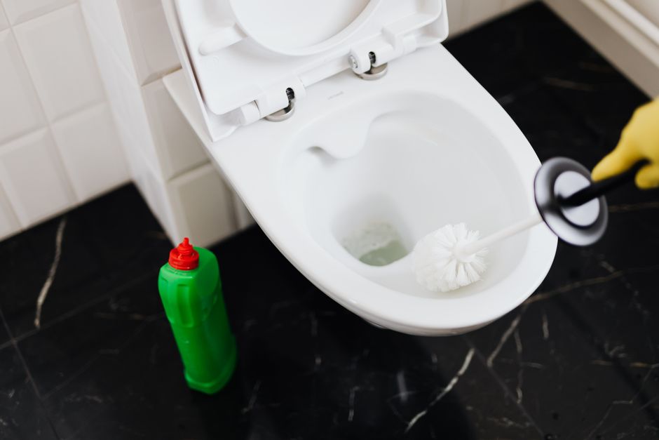 Pessoa limpando vaso sanitário com uma escova, em um ambiente de banheiro.
