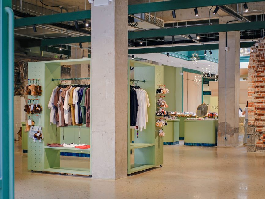 Interior de uma loja de roupas que combina elementos industriais e modernos, com prateleiras verdes e iluminação clean, promovendo um ambiente acolhedor para compras.