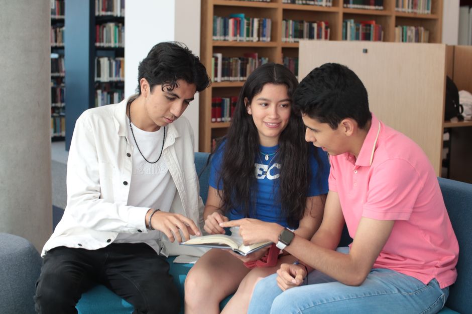 Grupo de jovens estudando e discutindo juntos em uma biblioteca, abordando temas relacionados à educação ou aprendizagem colaborativa.