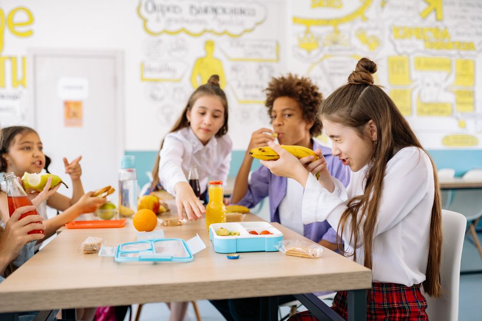 Grupo de crianças em um ambiente escolar, compartilhando frutas e lanches durante o intervalo.