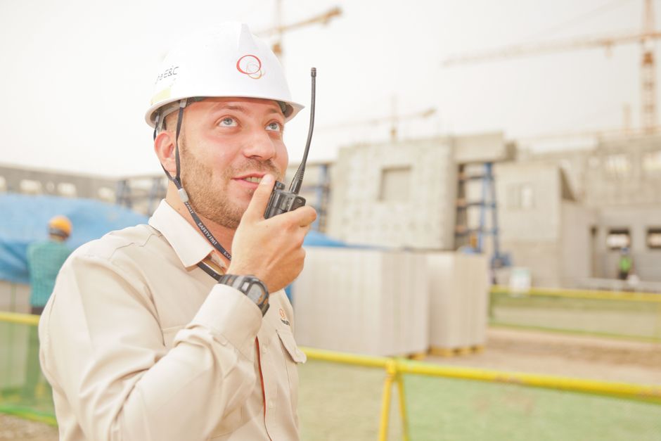 Engenheiro de construção civil usando rádio comunicador em um canteiro de obras, supervisionando o andamento do projeto.