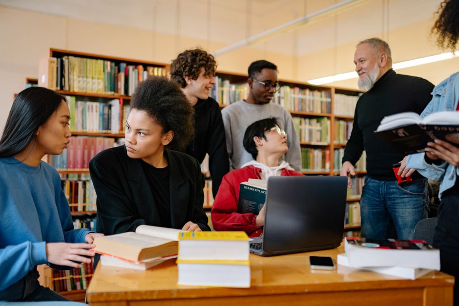 Grupo de pessoas estudando e discutindo em uma biblioteca, promovendo aprendizado e troca de conhecimentos.