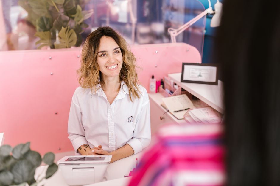 Mulher sorridente atendendo em uma recepção de estação de trabalho moderna e colorida, transmitindo acolhimento e atendimento ao cliente.