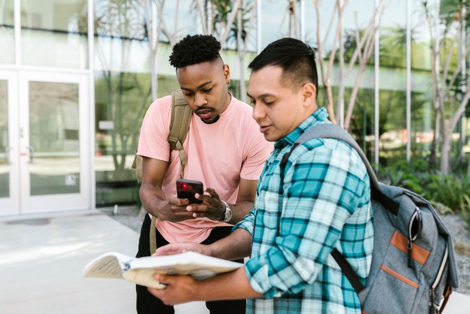 Dois estudantes discutem ou compartilham informações ao ar livre, com foco na troca de conhecimentos acadêmicos ou preparação para provas.