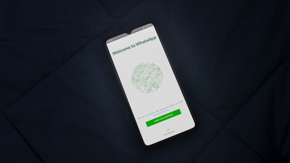 Imagem de um smartphone exibindo a tela de instalação do WhatsApp, situado sobre um colchão escuro, simbolizando uso de tecnologia móvel em ambientes cotidianos.