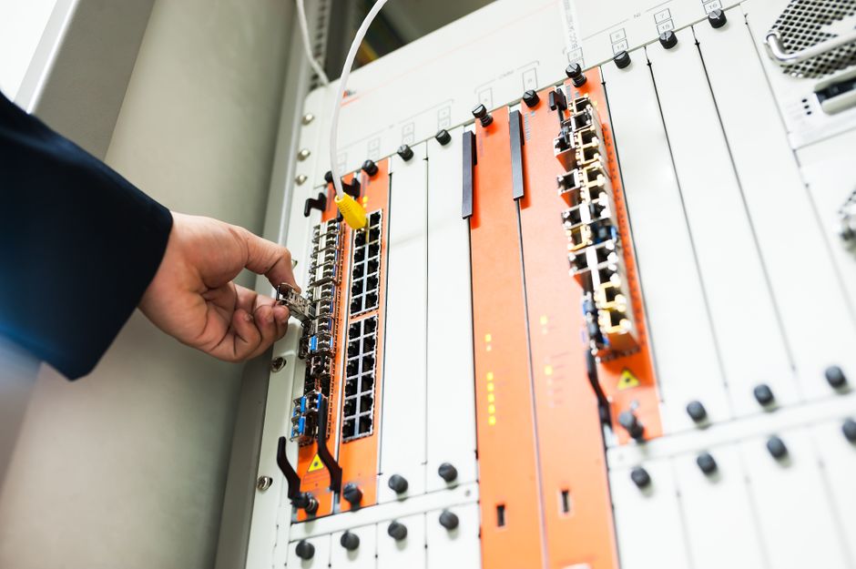 Profissional realizando manutenção em equipamento de automação industrial ou rede de comunicações de alta tecnologia.