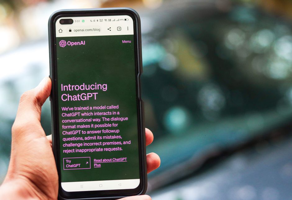 Pessoa segurando smartphone exibindo página sobre inteligência artificial e ChatGPT, com fundo desfocado ao ar livre.
