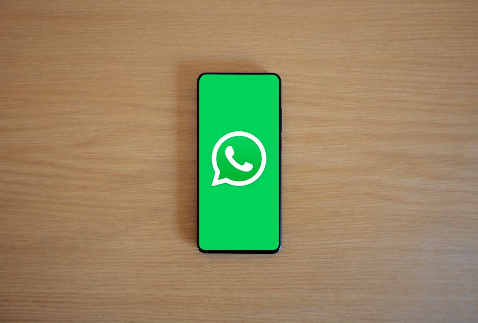 Imagem de um smartphone com o logo do WhatsApp na tela, sobre uma superfície de madeira, representando comunicação digital e mensagens instantâneas.