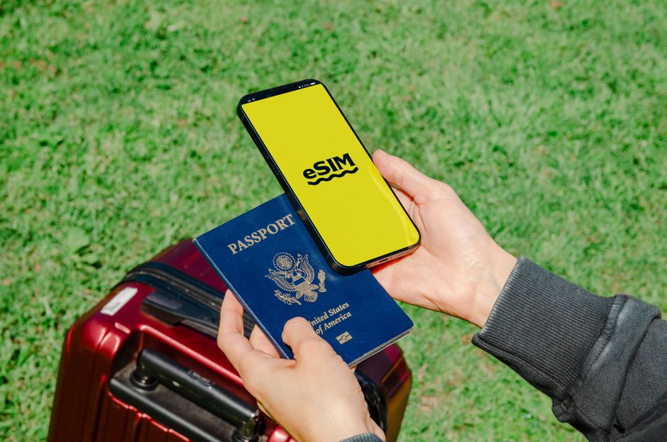 Pessoa verificando documentação de viagem com cartão de embarque digital em celular, ao lado de mala de viagem em ambiente ao ar livre.