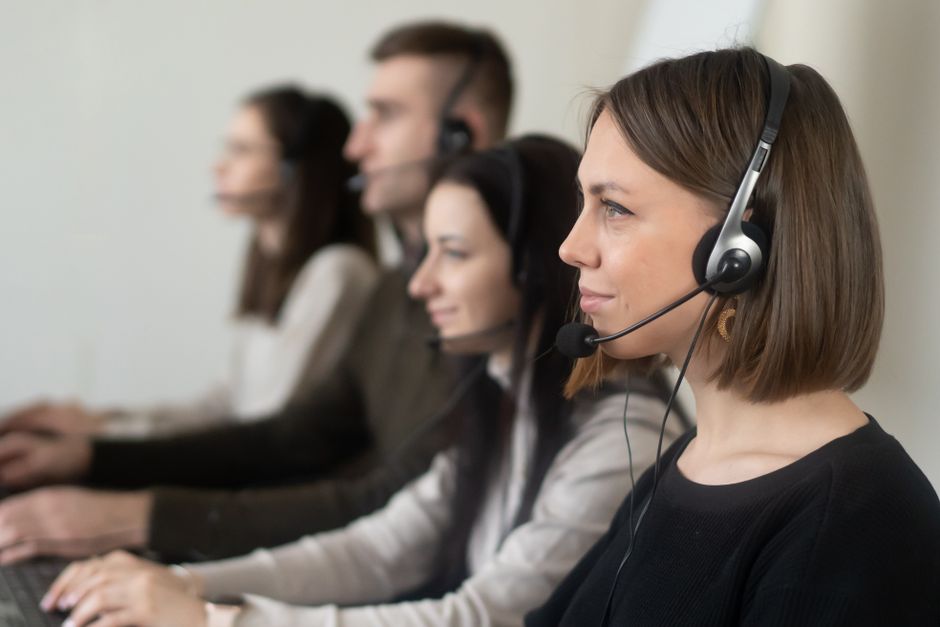 Equipe de atendentes ao telefone colaborando em um centro de suporte ou call center, focada no atendimento ao cliente.