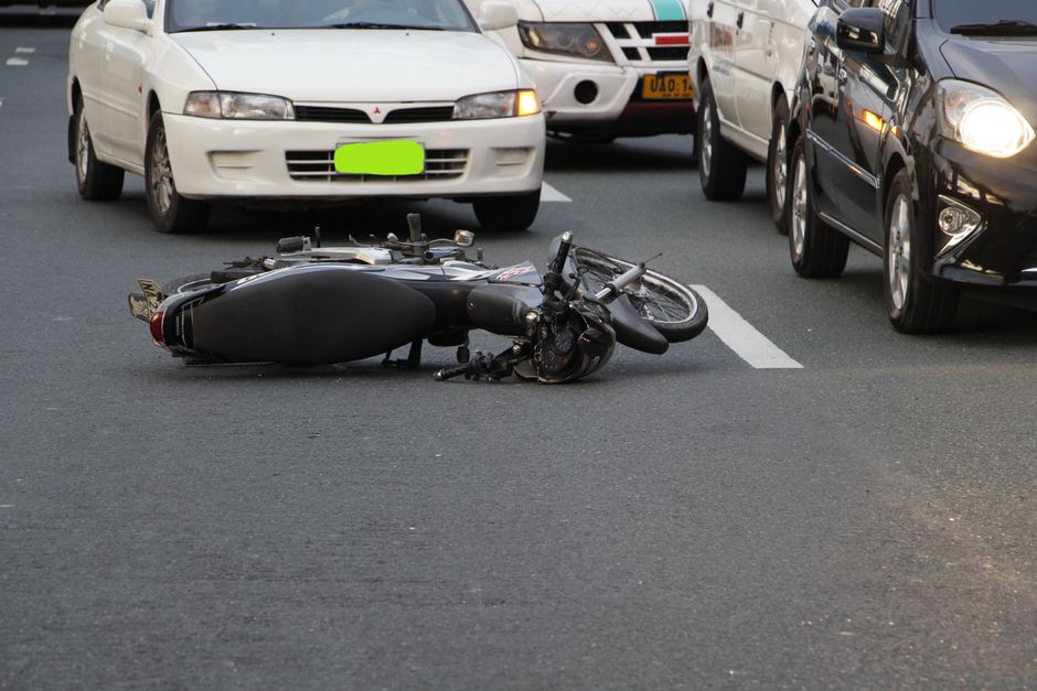 Imagem de um acidente de trânsito envolvendo uma motocicleta caída na pista, cercada por carros.