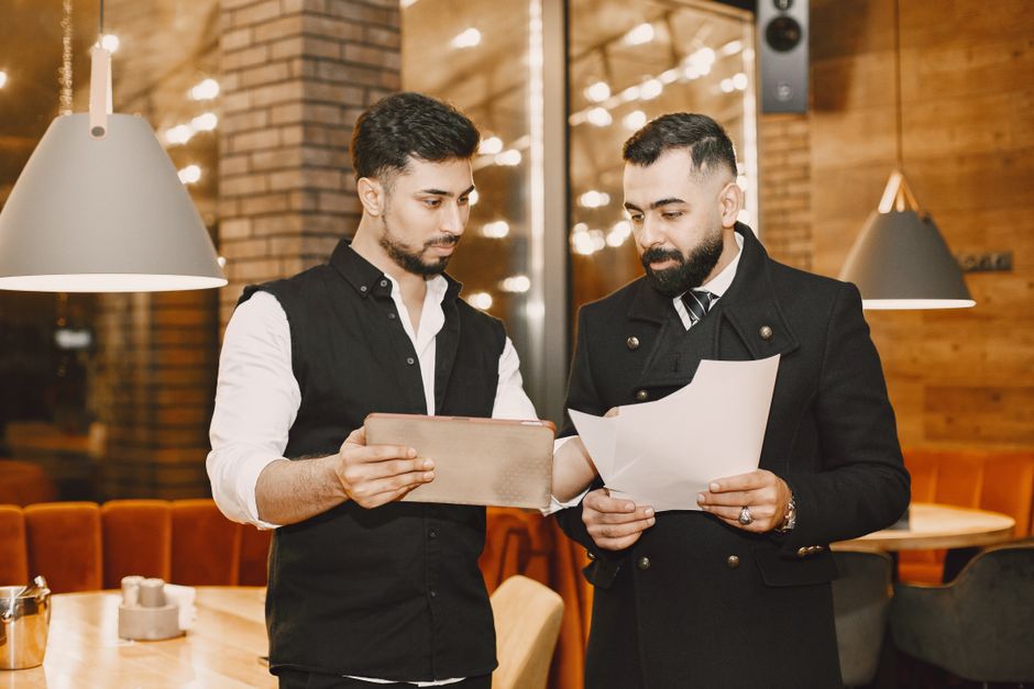 Dois homens discutindo estratégias de negócios em um ambiente de restaurante ou café com iluminação aconchegante e decoração em madeira.