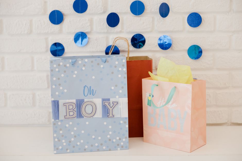 Três presentes de bebê decorados em uma parede de fundo com círculos de papel em tons de azul e dourado, ideal para celebrar chegada de um menino.