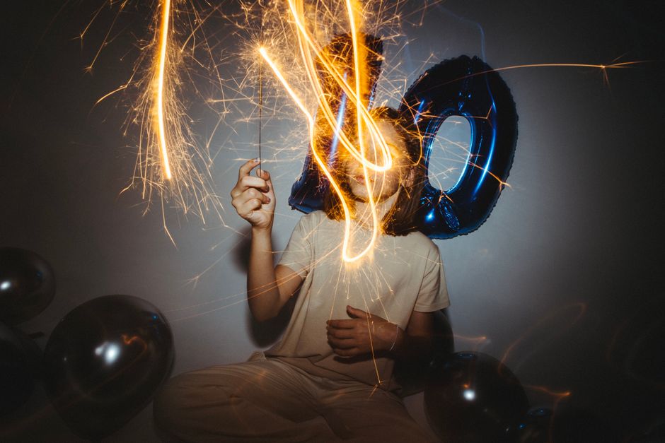Jovem comemorando uma celebração especial com balões, luzes e fogos de artifício, marcando uma ocasião de alegria e conquista.